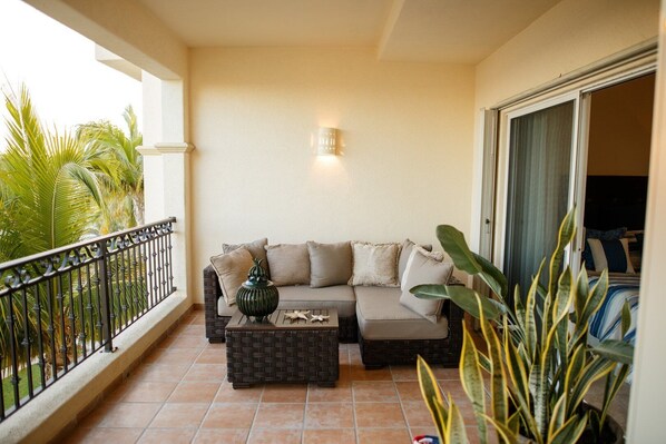 A balcony with a sofa and a coffee table, a potted plant, and a view of the outdoors. - Las Mañanitas LM E3402 (San José del Cabo)