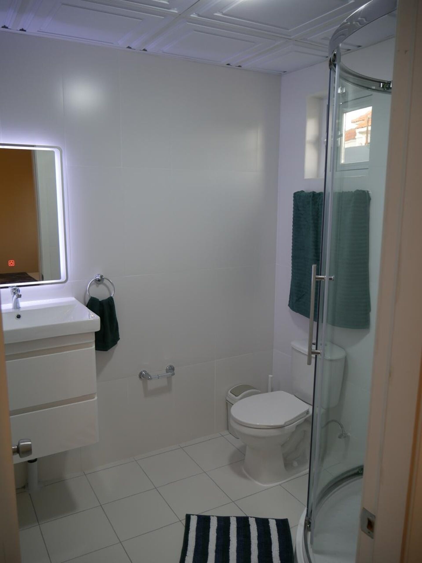 Un baño con lavamanos blanco, espejo, inodoro y cabina de ducha con mampara de cristal.