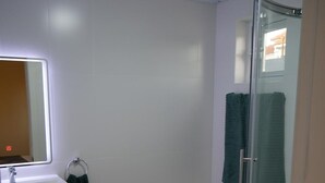 Un baño con lavamanos blanco, espejo, inodoro y cabina de ducha con mampara de cristal.