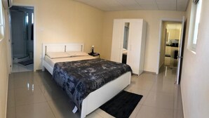Un dormitorio con cama, mesita de noche, armario y baño visible a través de una puerta abierta.