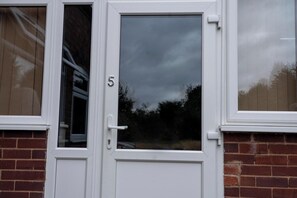 A white door with a glass panel, a visible number '5', and a reflection of trees and sky.