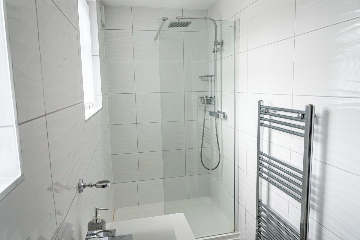 Ein modernes Badezimmer mit einer gläsernen Duschkabine, einem weißen Waschbecken und einem chromfarbenen Handtuchhalter.