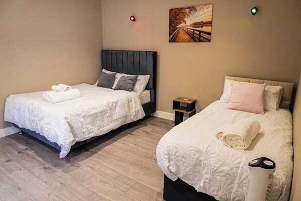Two beds with white linens, a painting on the wall, and a heater on the floor.