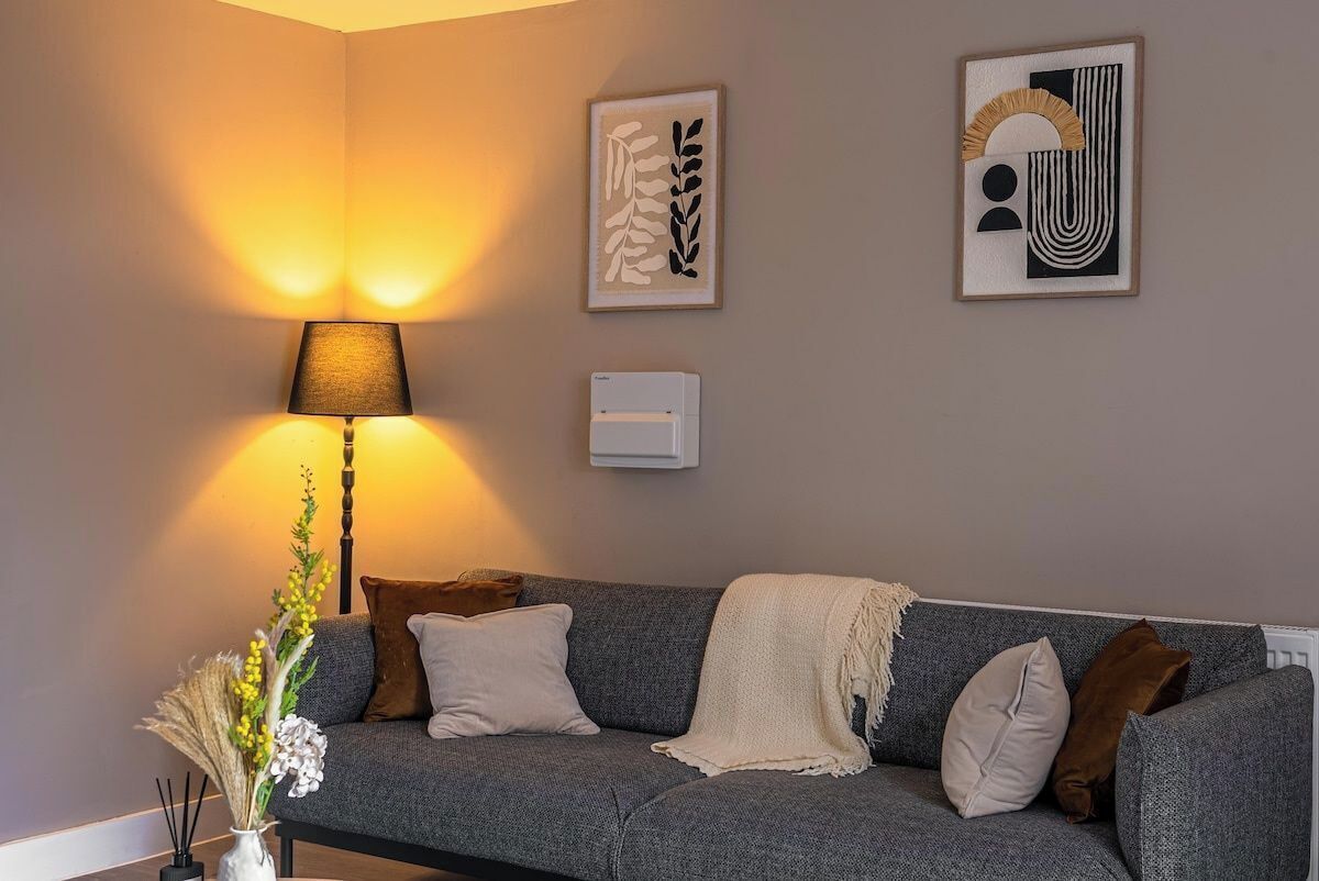 A living room with a grey sofa, a lamp, and wall art.