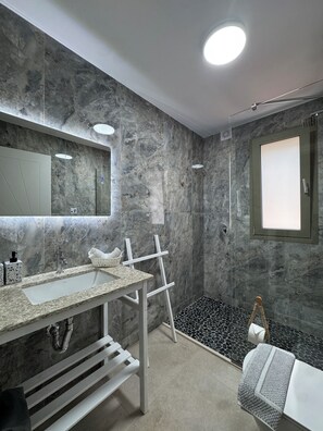 A modern bathroom with a marble wall, a large mirror, a sink, and a shower area.