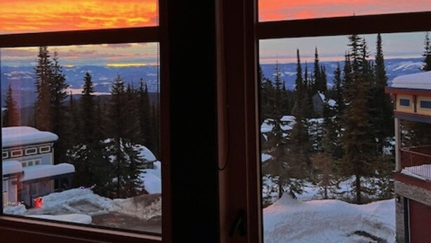 Une pièce dotée de deux fenêtres donnant sur un paysage enneigé et un coucher de soleil.