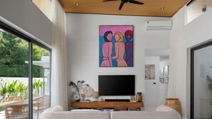 A modern living room with a large flat-screen TV, a sofa, and a ceiling fan.