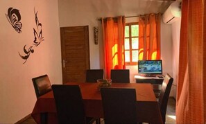 A dining area with a wooden table and chairs, a television on a stand, and orange curtains. - Miramar cabin a few meters from the beach (Playa Grande)