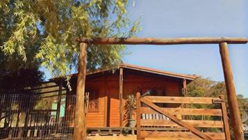 A wooden cabin with a metal gate, surrounded by a fence and trees.