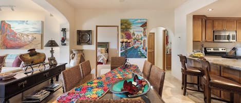 A dining area with a long table, wicker chairs, and a colorful table runner.