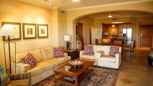 A living room with a sofa, armchair, coffee table, and decorative pillows. There is a dining area in the background with a chandelier and a large vase. - Las Mañanitas LM F4205 (San José del Cabo)