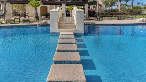 A pool with a clear blue water surface, stone steps leading into the pool, and a covered area with tables and chairs.