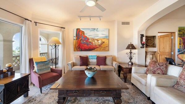 A spacious living room with a large painting, a ceiling fan, and a view through a glass door.