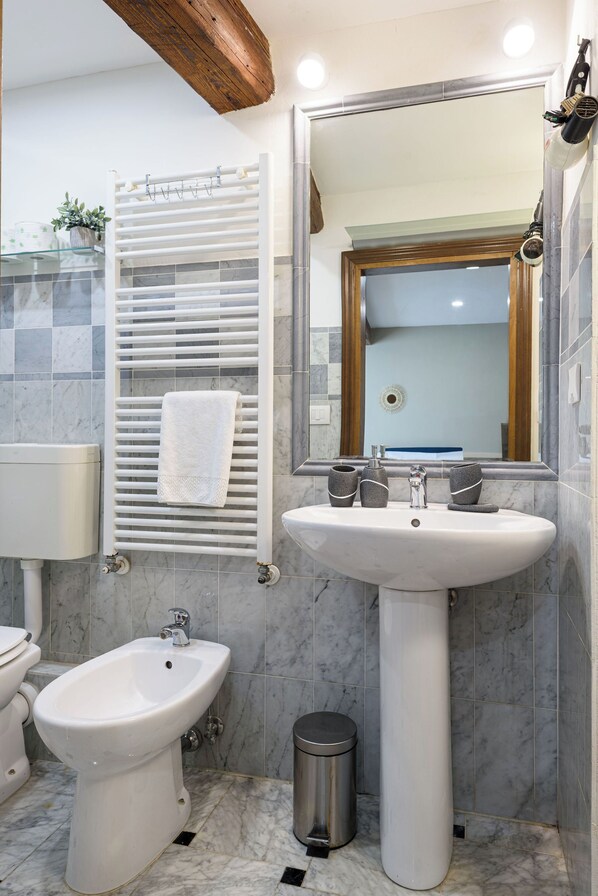 A bathroom with a pedestal sink, bidet, and a towel rack with a towel.