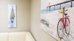 A room with a beige couch, a painting of a bicycle on a beach, and a sailboat painting on the wall. - Santo Spirito: Florence's Residential Soul apartment (Firenze)