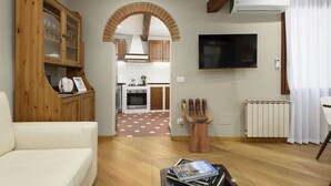 A living room with a sofa, a wooden cabinet, a TV mounted on the wall, and a kitchen visible through an archway. - Santo Spirito: Florence's Residential Soul apartment (Firenze)