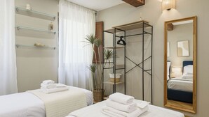 A hotel room with two beds, a large mirror, and a shelving unit with towels. - Santo Spirito: Florence's Residential Soul apartment (Firenze)