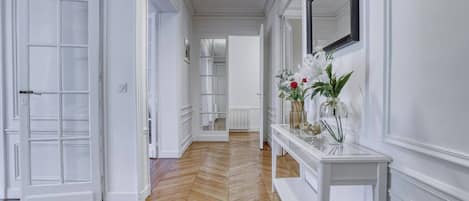 A hallway with a wooden herringbone floor, white walls, and a white console table with vases.