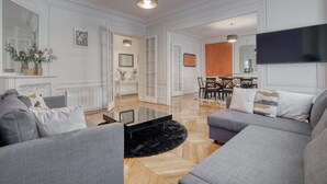 Un salón amplio con sofás grises, una mesa de centro y una chimenea. En el fondo, hay un comedor con una mesa y sillas.