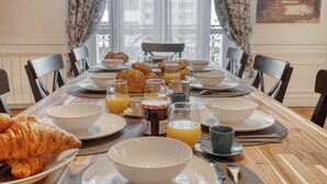 Un desayuno con croissants, zumo de naranja y café sobre una mesa con sillas alrededor.