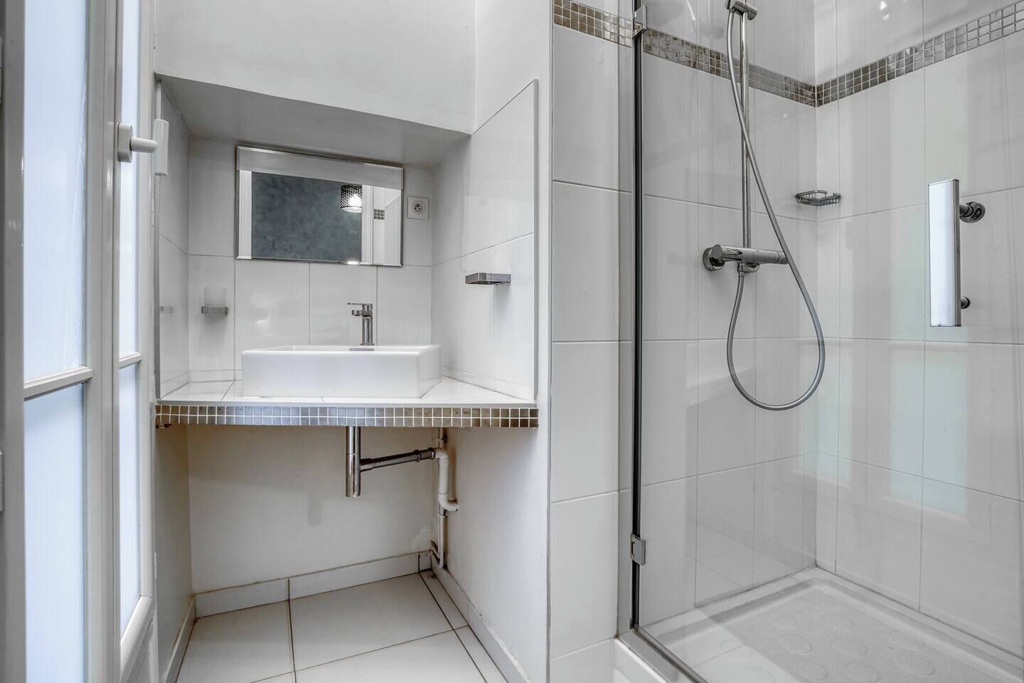 A modern bathroom with a glass-enclosed shower, a sink with a mirror above it, and tiled walls.