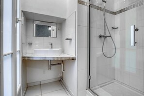 A modern bathroom with a glass-enclosed shower, a sink with a mirror above it, and tiled walls. - [120 m2] Luxury Eiffel Signature (Paris)