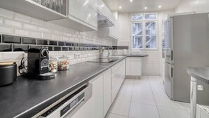 Una cocina moderna con armarios blancos, encimera negra y refrigerador de acero inoxidable.