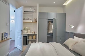 A bedroom with a bed, a wardrobe, a shelf with decorative items, and a bedside lamp. - Express by M Village Dinh Cong Trang, a brand of Modern Village Lifestyle (Ho Chi Minh City)