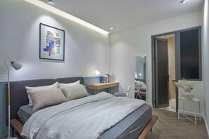 A modern bedroom with a bed, bedside table, lamp, and a framed picture on the wall. - Express by M Village Dinh Cong Trang, a brand of Modern Village Lifestyle (Ho Chi Minh City)