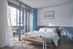 A modern bedroom with a bed, bedside tables, a window with curtains, and a framed picture on the wall. - Express by M Village Dinh Cong Trang, a brand of Modern Village Lifestyle (Ho Chi Minh City)