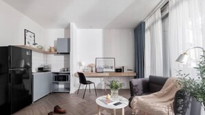 Una cocina moderna con un refrigerador negro, un comedor con mesa y sillas, y una sala de estar con un sofá y una lámpara.