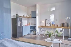 A modern kitchen with a refrigerator, microwave, and a dining area with chairs and a table. - Express by M Village Dinh Cong Trang, a brand of Modern Village Lifestyle (Ho Chi Minh City)