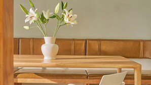 Una mesa de madera con un jarrón blanco lleno de flores blancas.
