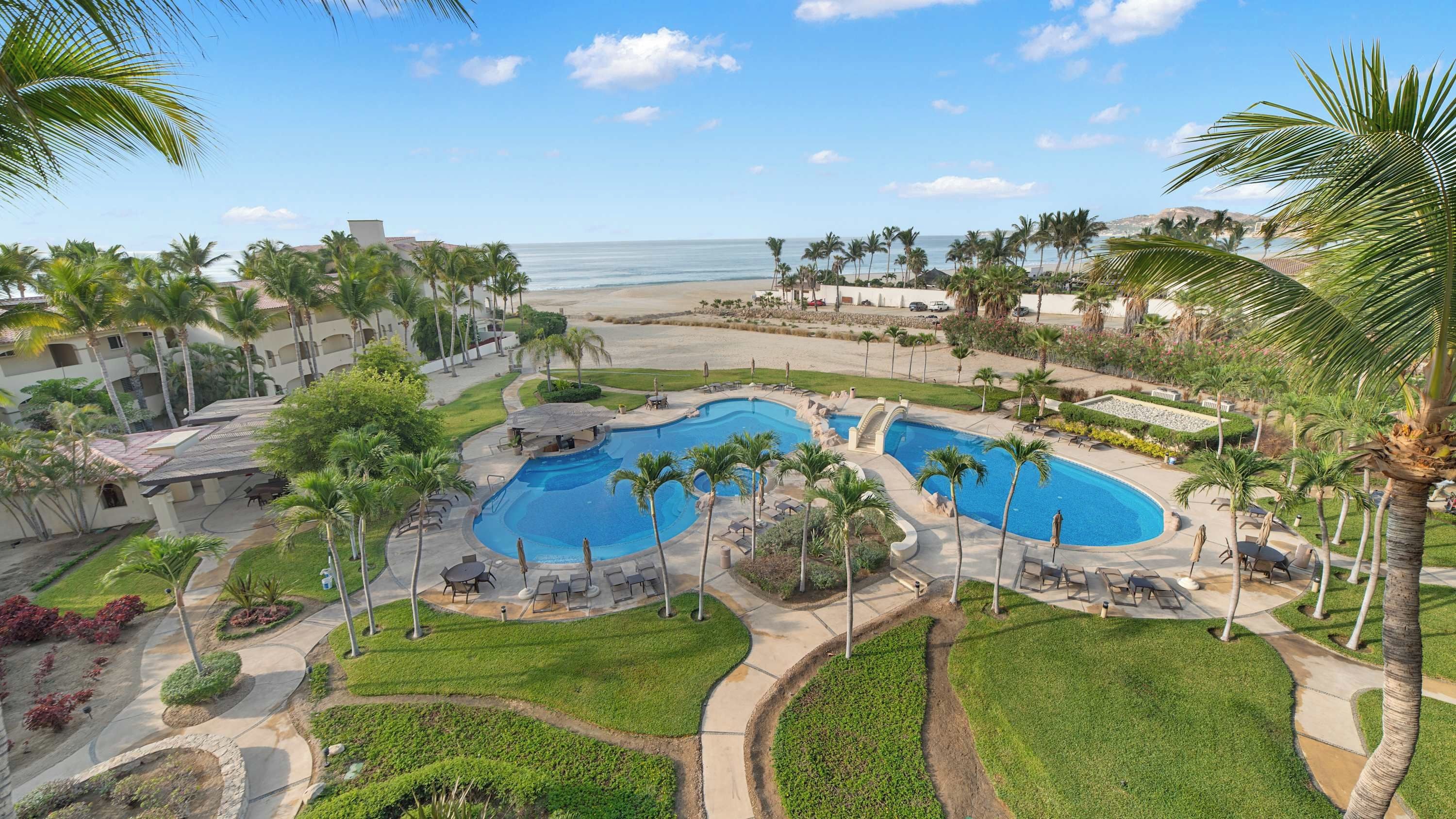 Un resort con un amplio área de piscina, palmeras y vista al océano.