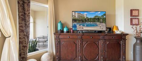 Una habitación con una televisión de pantalla grande montada en un mueble de madera, una ventana con cortinas, una cama y una planta pequeña.
