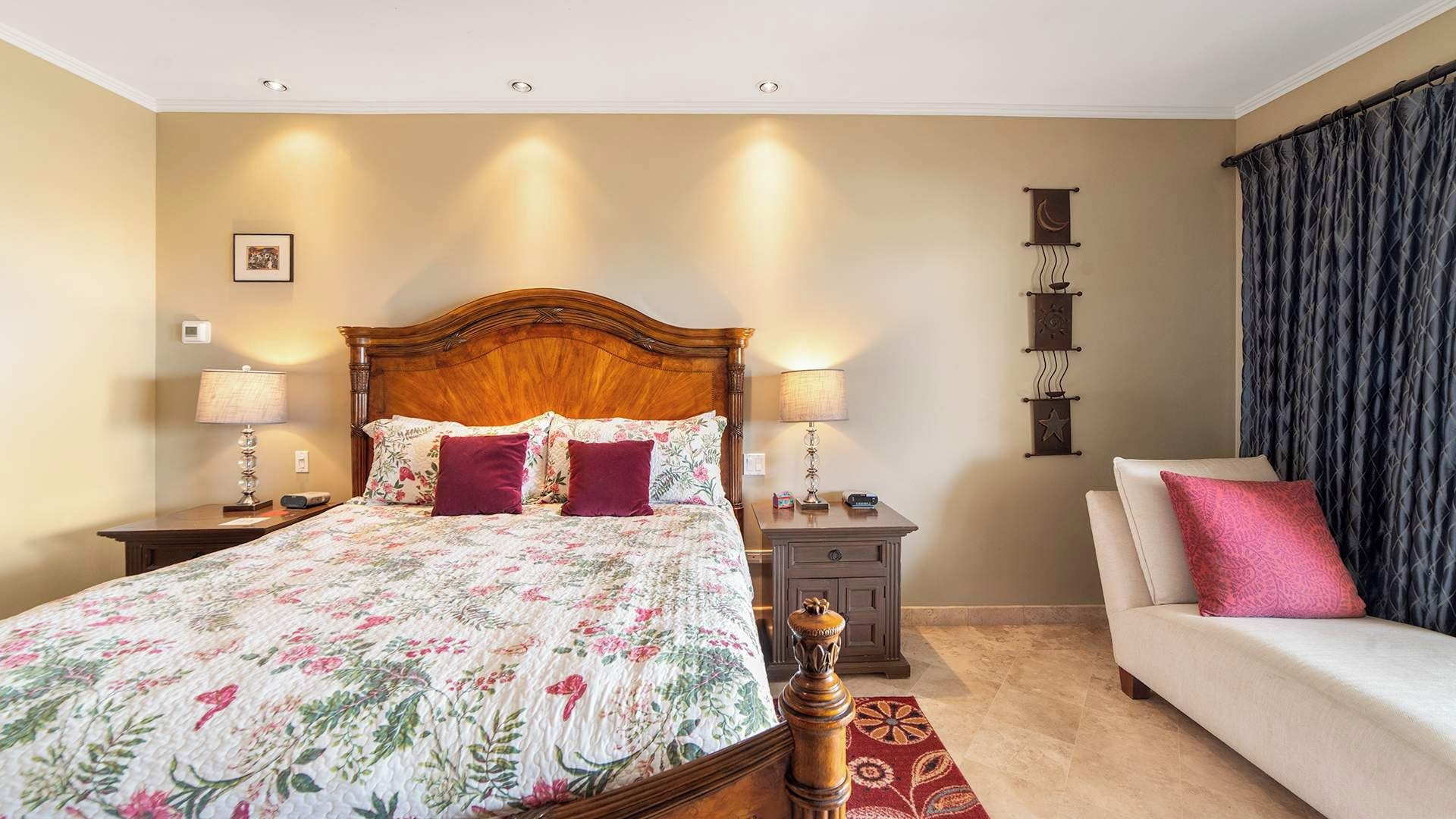 A hotel room with a large bed, bedside lamps, a nightstand, a sofa, and a decorative wall piece.