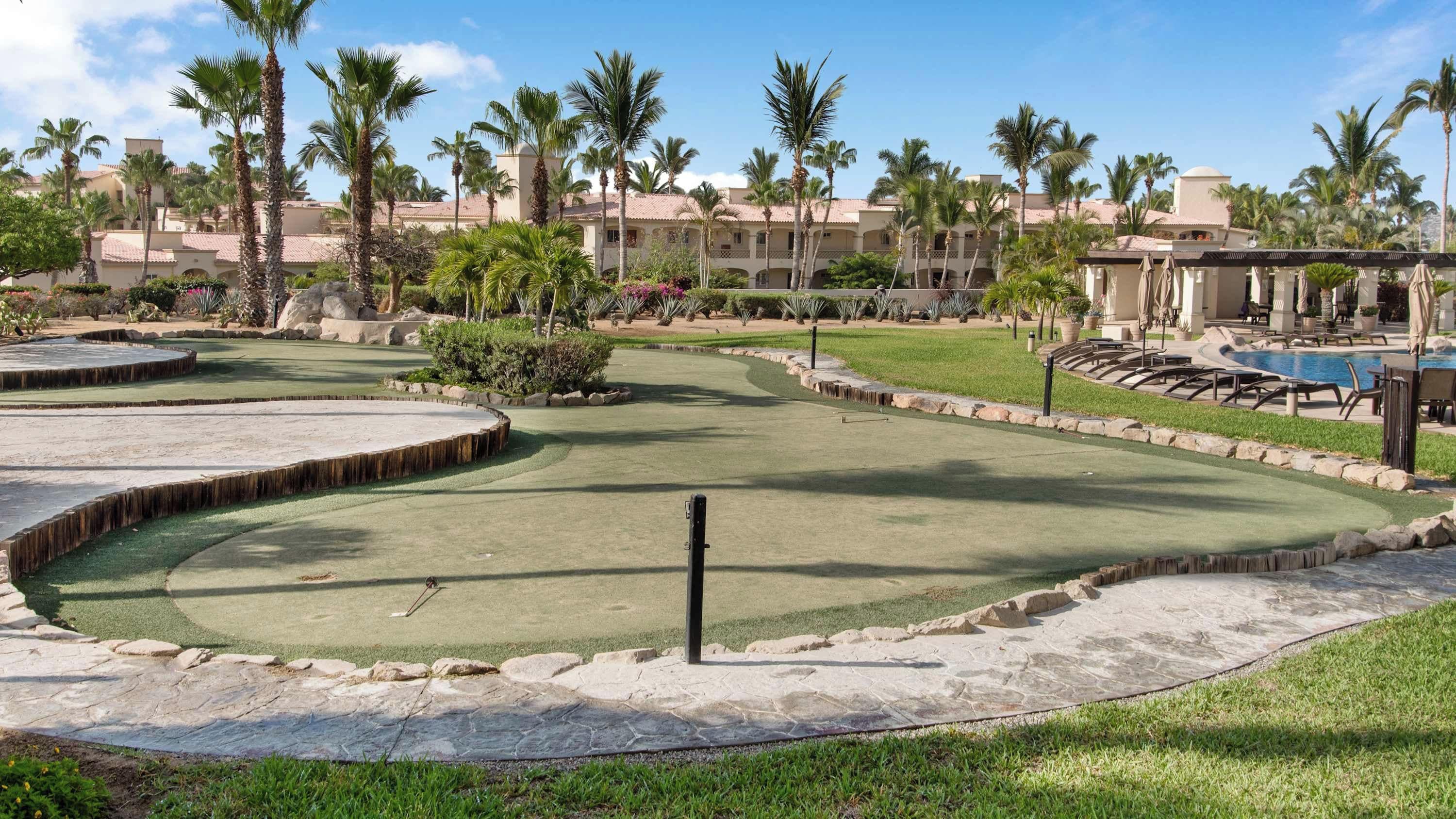 Ein Golfplatz mit Poolbereich, Palmen und einem Gebäude mit Ziegeldach.