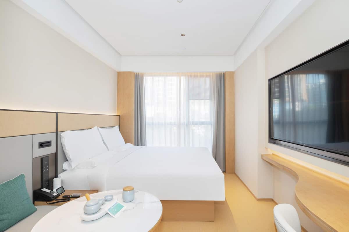 Ein Hotelzimmer mit Bett, Nachttisch, Fernseher und einem Fenster mit Vorhängen.