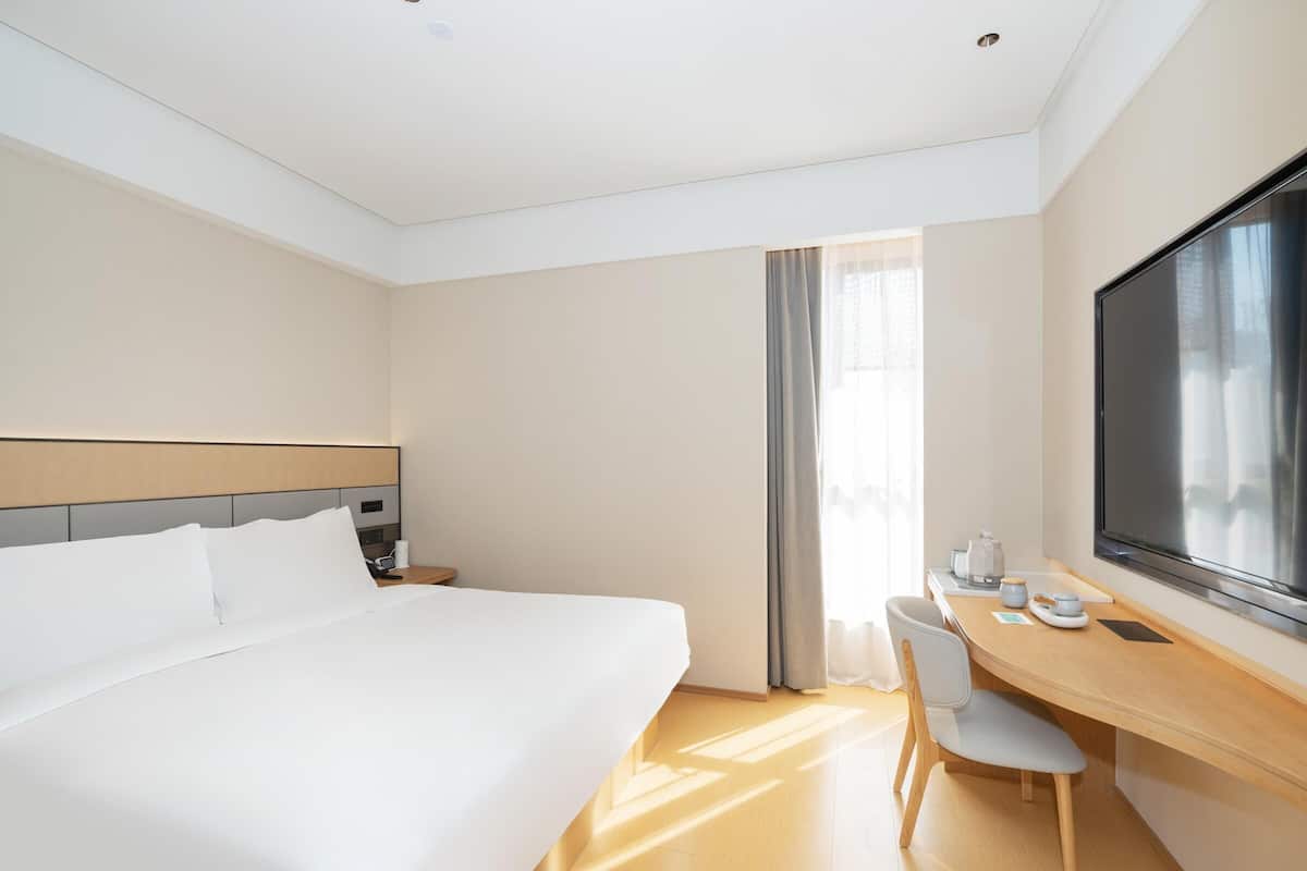 Ein Hotelzimmer mit einem großen Bett, einem Schreibtisch mit Stuhl, einem Flachbildfernseher und einem Fenster mit Vorhängen.