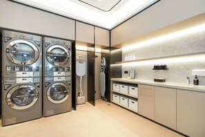 A modern laundry room with two front-loading washing machines, a drying machine, and a built-in ironing board. - Ji Hotel Guangzhou Fangcun Huadiwan (Guangzhou)