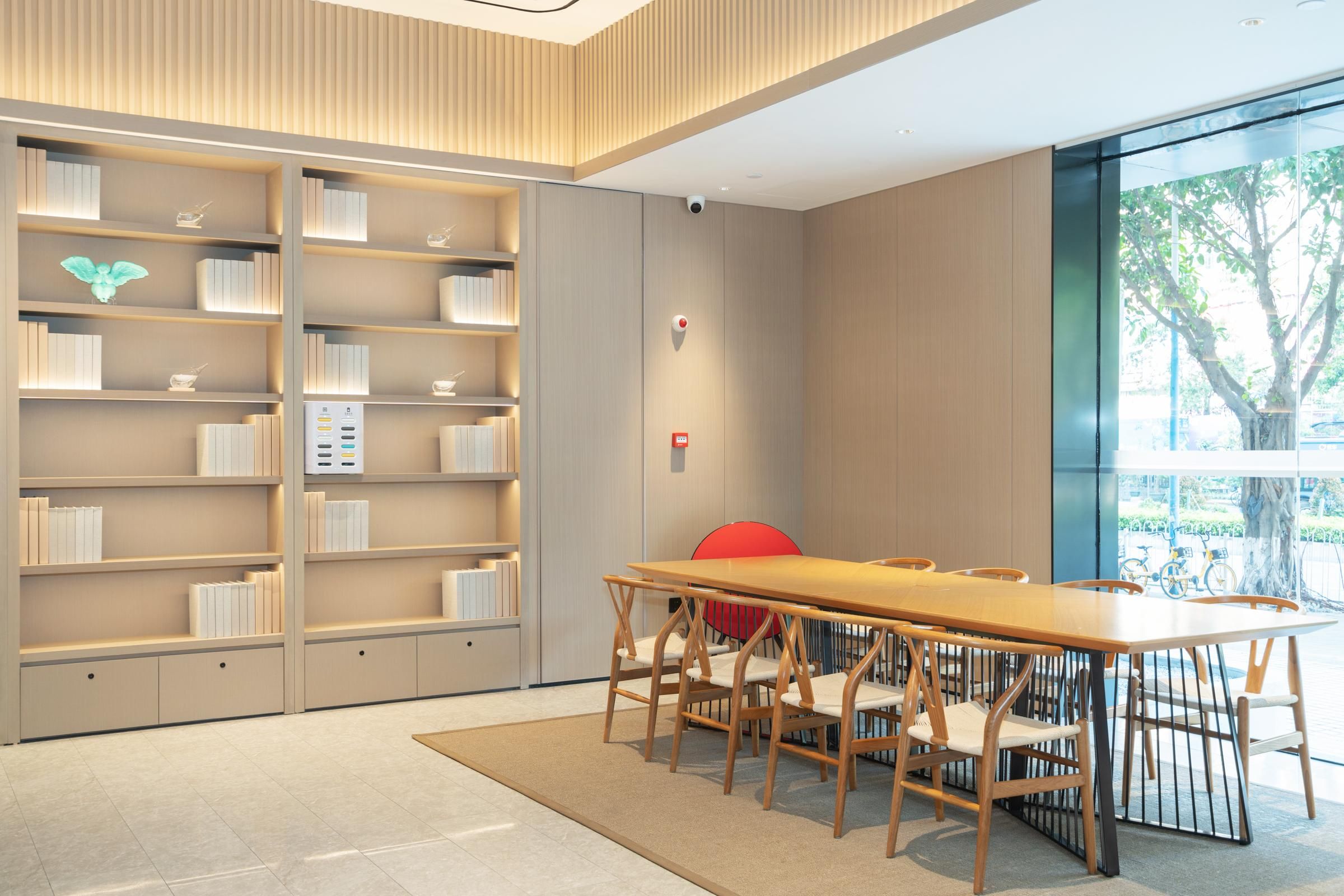 Une bibliothèque moderne avec une longue table en bois et des chaises, entourée d’étagères.