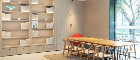 A modern library with a long wooden table and chairs, surrounded by bookshelves.