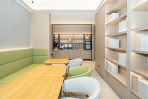 A modern, well-lit room with a green sofa, wooden tables, and light-colored chairs. A kitchen area with appliances and a refrigerator is visible in the background. - Ji Hotel Guangzhou Fangcun Huadiwan (Guangzhou)