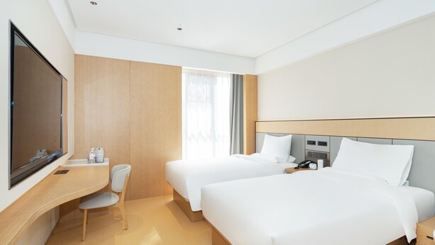 Une chambre d’hôtel avec deux lits, un bureau, une chaise, une télévision et une fenêtre avec des rideaux.