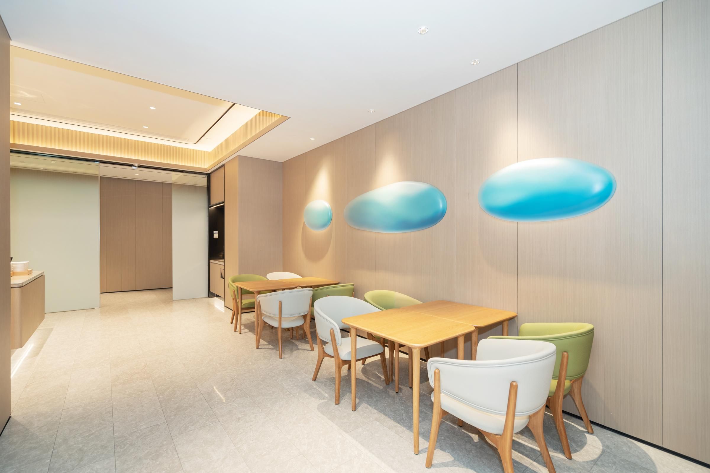 A modern dining area with wooden tables and chairs, a light-colored floor, and a wall with abstract blue shapes.