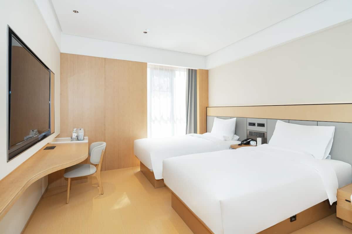 Ein Hotelzimmer mit zwei Betten, einem Schreibtisch, einem Sessel, einem Fernseher und einem Fenster mit Vorhängen.