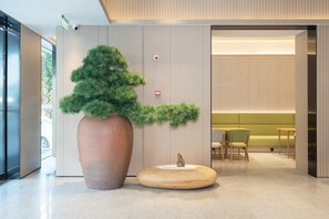 A modern interior with a large potted plant, a wooden table, and seating area. - Ji Hotel Guangzhou Fangcun Huadiwan (Guangzhou)