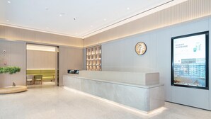 Un espace d’accueil moderne doté d’un comptoir en marbre, d’un écran numérique et d’un coin salon avec des chaises et un canapé.