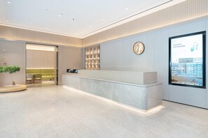 A modern reception area with a marble counter, a digital display, and a seating area with chairs and a sofa. - Ji Hotel Guangzhou Fangcun Huadiwan (Guangzhou)