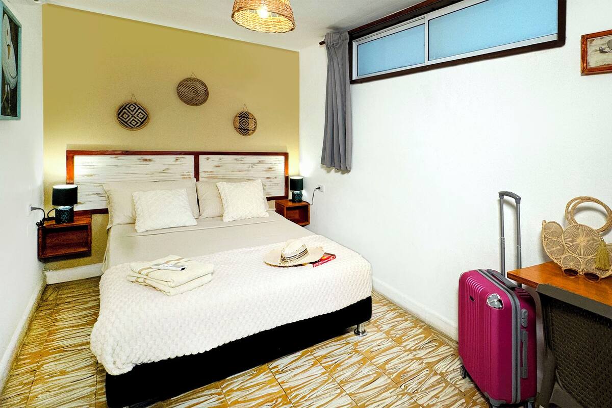 A hotel room with a bed, a suitcase, and a window with curtains.